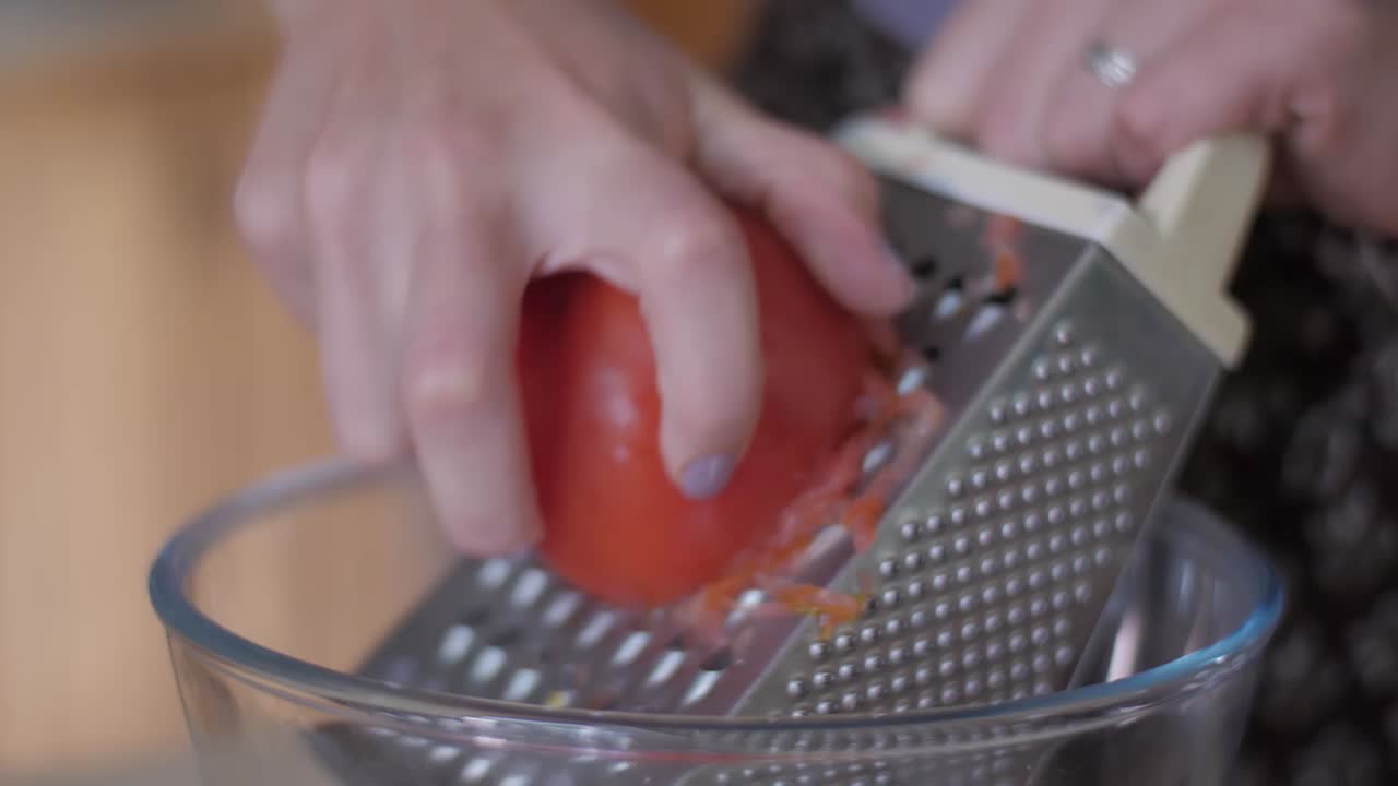 Hand grating a fresh tomato into a bowl