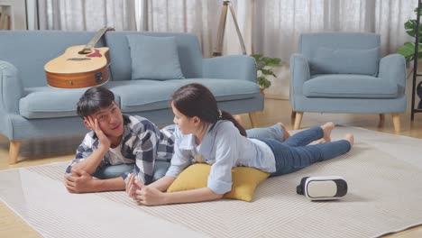 full body of asian teen couple speaking, laughing, and enjoying time together while lying on carpet on the floor at home