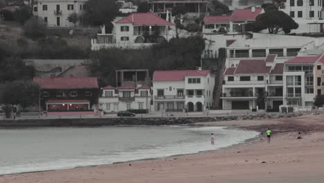 Gente-En-La-Playa-De-Sao-Martinho-Do-Porto-En-Leiria,-Portugal---Hermosas-Casas-De-Pueblo-En-El-Fondo---Tiro-Estático,-Cámara-Lenta