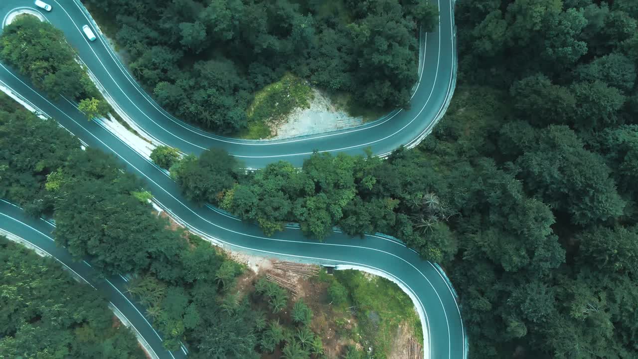 Toma aérea en 4K de coches circulando por una carretera con curvas en la ladera de una montaña