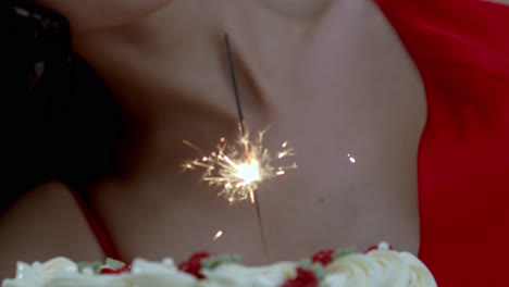 un pastel de cumpleaños con un fuegos artificiales en él para la chica que celebra en un vestido rojo