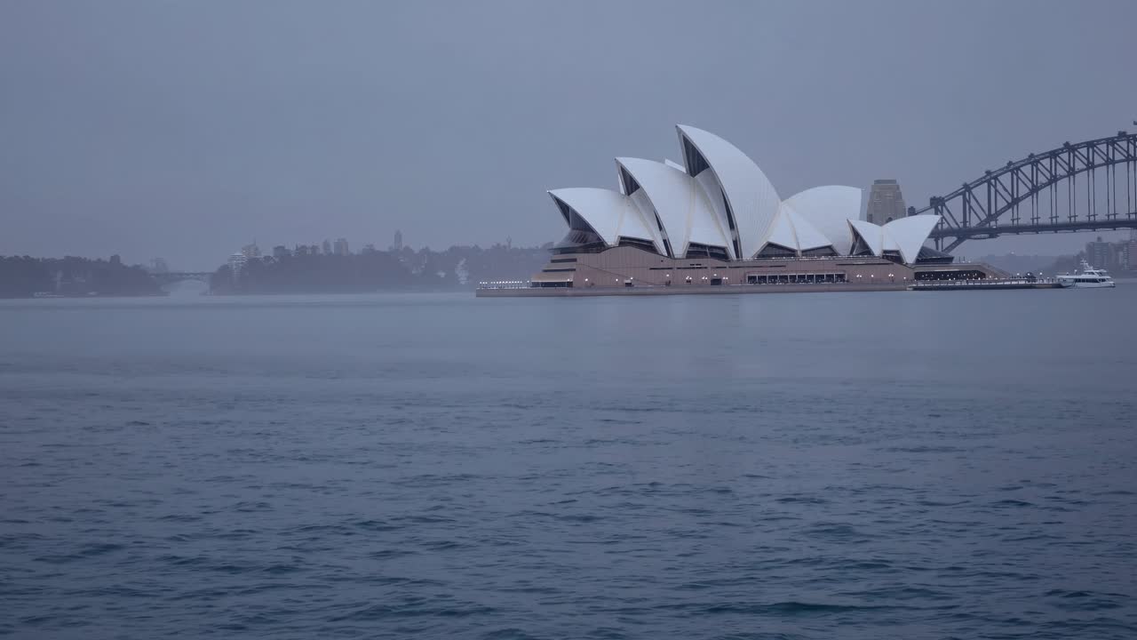 A serene wide-angle video captures the iconic Sydney Opera House and Harbour Bridge at dusk
