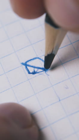 young man draws image and breaks slate of blue pencil on checkered paper sheet extreme close view