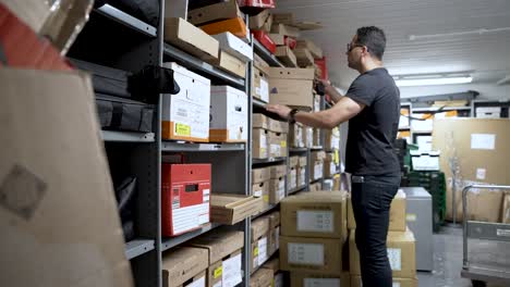 Hombre-Europeo-Con-Gafas-Organizando-Cajas-En-Un-Trastero-Lleno-De-Estantes-Y-Artículos-Varios.