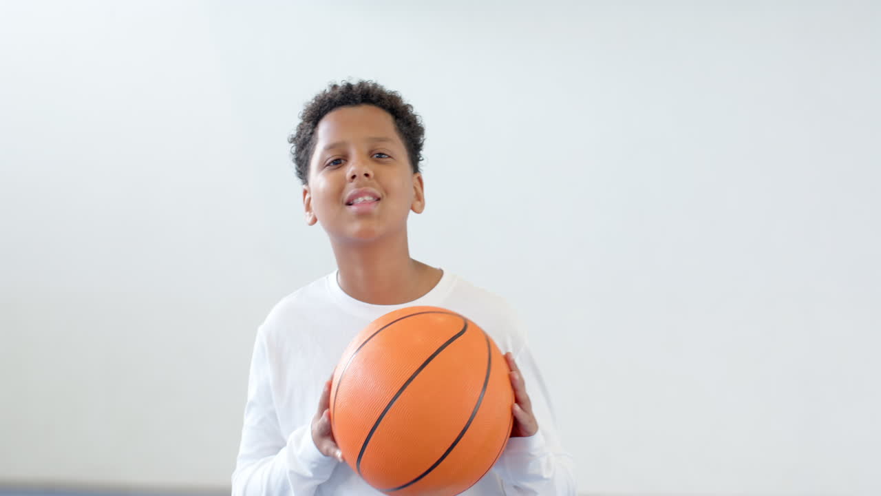Young boy focusing on basketball practice in school gym, holding ball, copy space