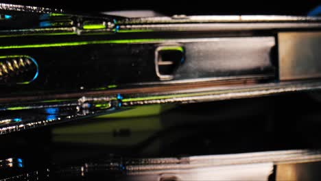 a stylized and dramatic panning close up of the inside of a stapler loaded with staples illuminated by a blue and green light with black background