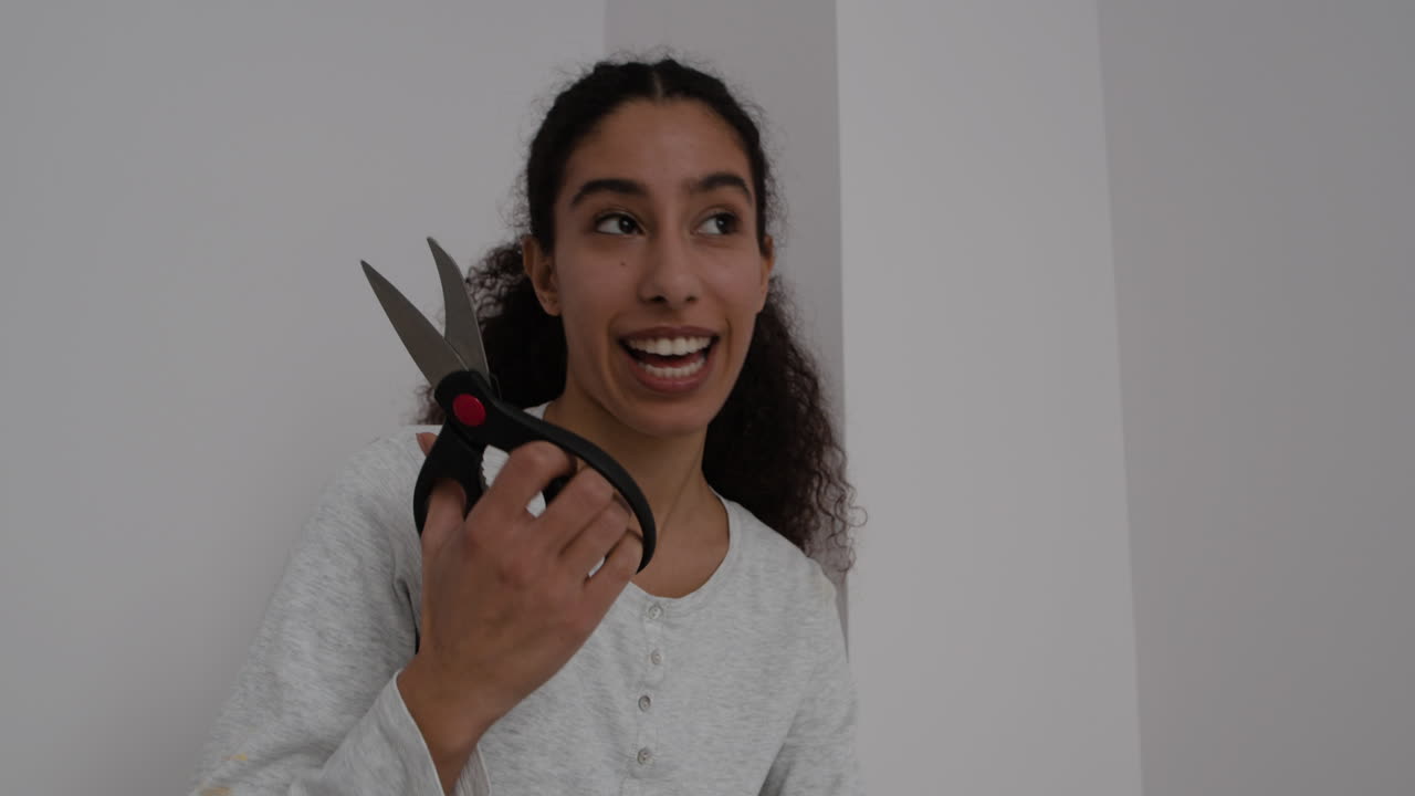 Young woman with curly hair holding scissors and smiling