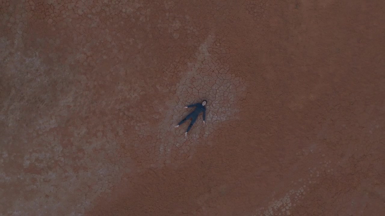 Vista a volo d'uccello di un uomo sdraiato su una vasta distesa di terreno desertico crepato