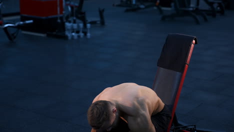 bodybuilder with perfect body and strong hands trains with dumbbells. dark background of modern gym. slow motion.