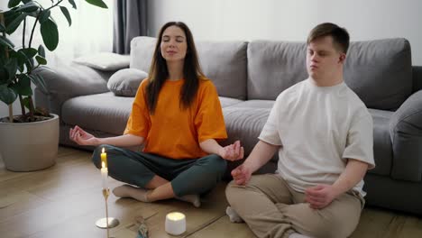 Portrait-of-a-woman-assisting-guy-with-down-syndrome-doing-in-meditating-at-home,-slow-motion