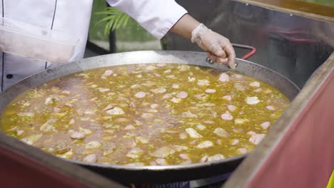 Chef-Wearing-White-Costume-Cooking-Paella,-The-Popular-Spanish-Dish