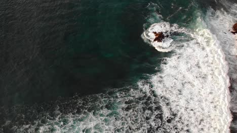 Aerial-view-of-waves-splashing-on-the-rocks-in-Uluwatu,-Bali