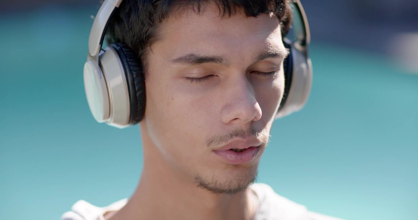 Uomo afroamericano che ascolta musica in cuffia, con gli occhi chiusi, che unisce i palmi, rilassandosi a bordo piscina.
