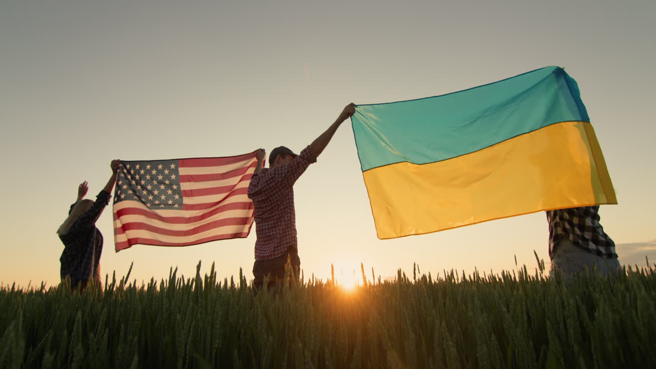 A group of happy friends raises the flag of the United States and the flag of Ukraine over their heads.