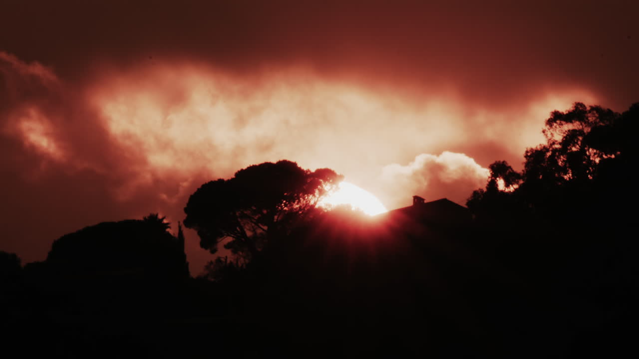 Un sole rosso incandescente parzialmente coperto da nuvole scure al tramonto