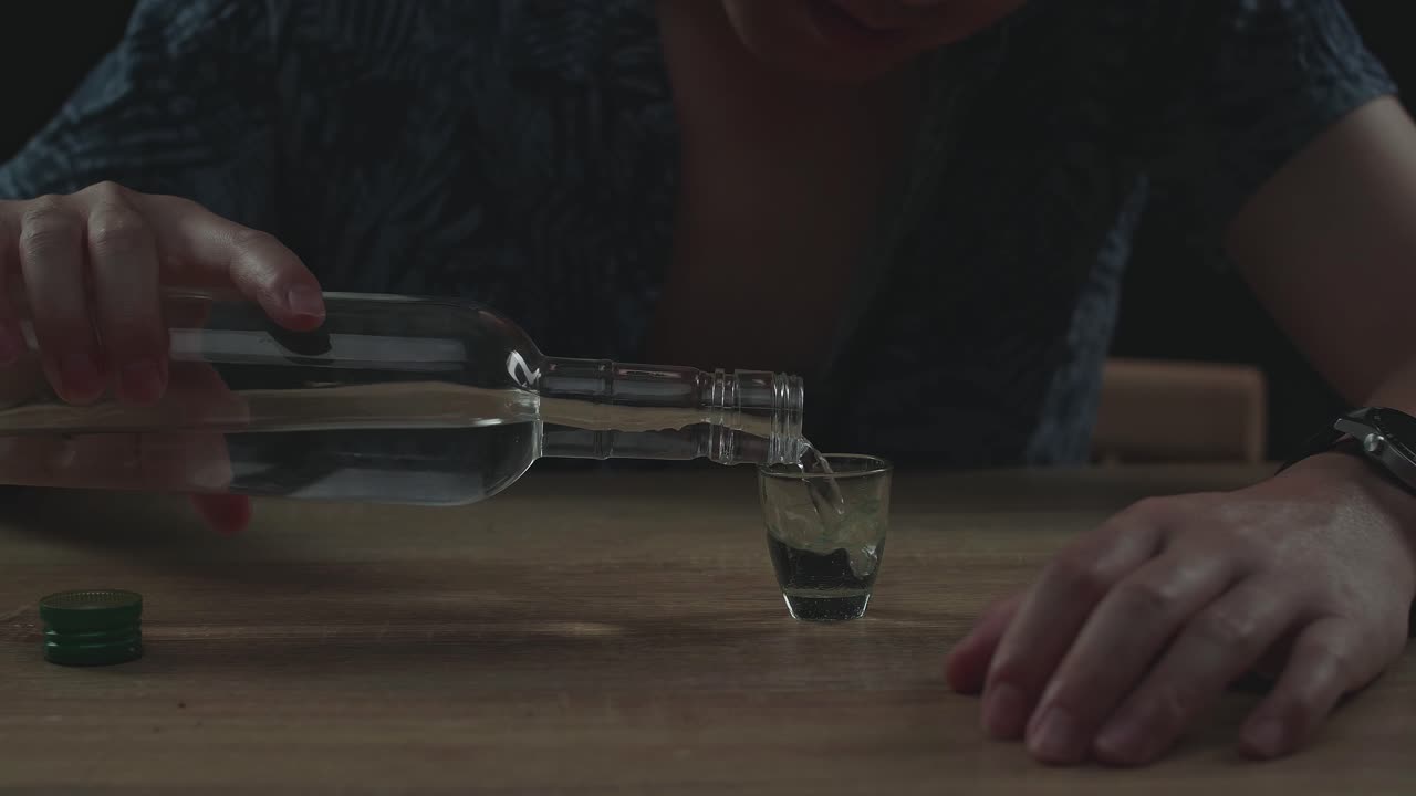 술에 취한, 우울한 아시아 남자가 검은 바탕에서 술을 마시기 전에 글라스에 보드카를 부어