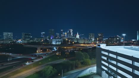 car park with busy highway at night in atlanta city, georgia. aerial forward wide shot. skyline and skyscrapers in distance. lighting buildings of downtown.