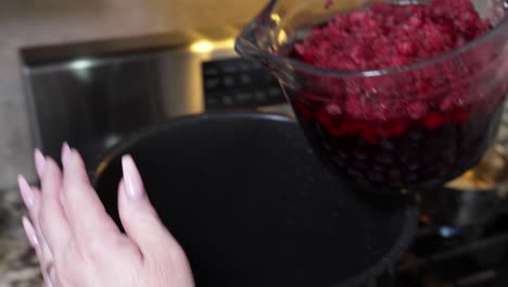 dumping a bowl full of raspberries and blueberries into a pot on the stove to make jam - slow motion