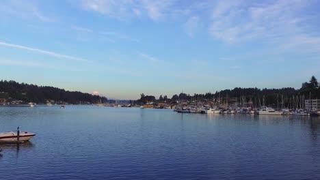 sailboats moored at the docking terminal of gig harbor marina and boatyard in washington with distant view of the snowy mount rainier peak - wide panning shot