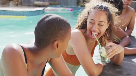two happy female friends having drinks laughing in pool