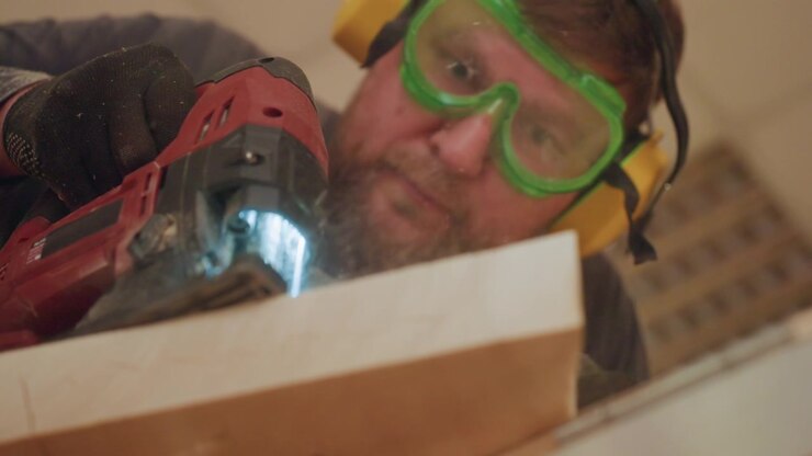 Close up shows person using electric saw to cut through thick lumber creating fine sawdust particles. focus remains on interaction between hand held power tool and wooden material throughout
