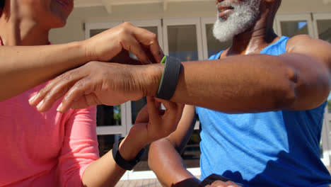 Front-view-of-mature-black-woman-helping-man-to-wear-fitness-band-in-back-yard-of-their-home-4k