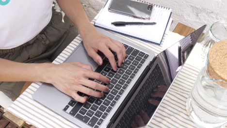 Top-view-woman-working-on-her-laptop,-typing-on-a-keyboard-outside-at-a-cafe-table