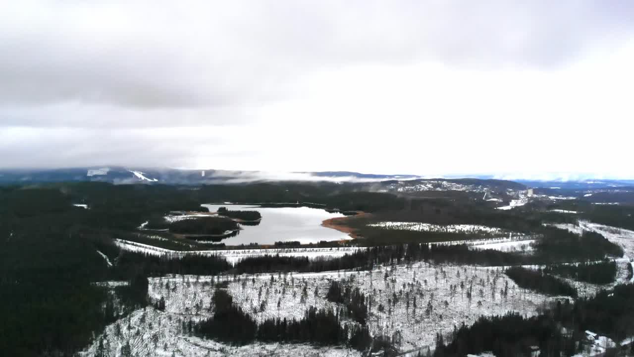 Ilmakuva lumisesta järvestä talvisessa metsässä
