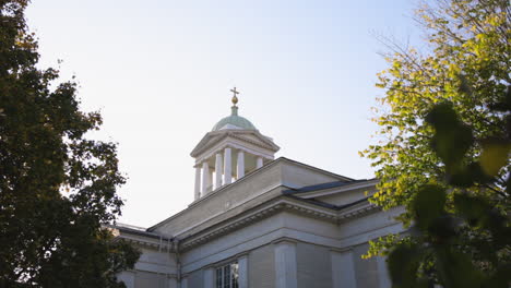 helsinki old church - white pillared steeple with a golden cross catches the sun framed by nearby trees