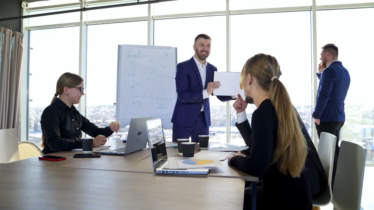 Business meeting in modern office centre in the city. Positive entrepreneur speaking to a group of young people sitting at the table in office.