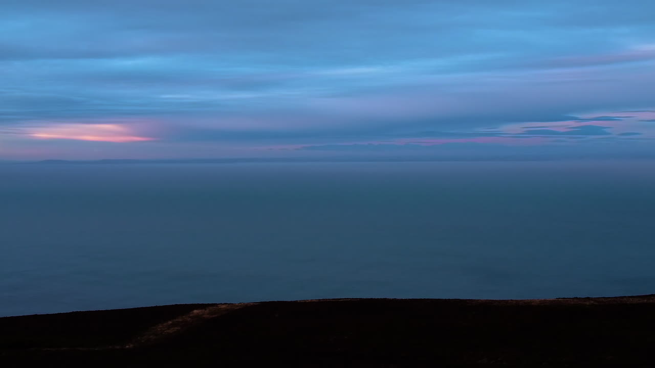 Paesaggio scuro in movimento orbitale con nuvole vivaci e colorate sul mare con ricche tonalità di blu e arancione. Clip di volo di drone aereo.