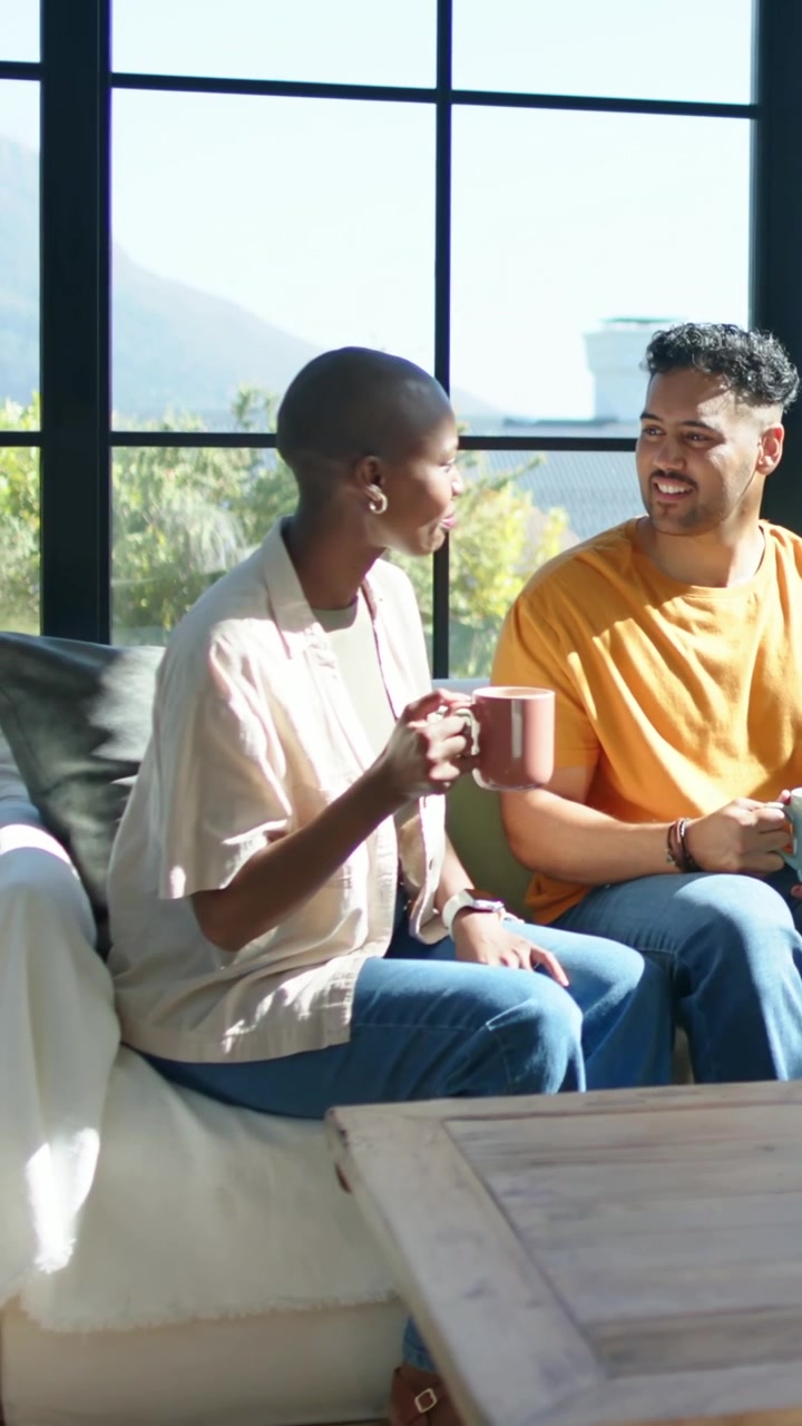 Vertical video: Talking woman sipping pink mug, starting chat at home, man smiling with blue mug