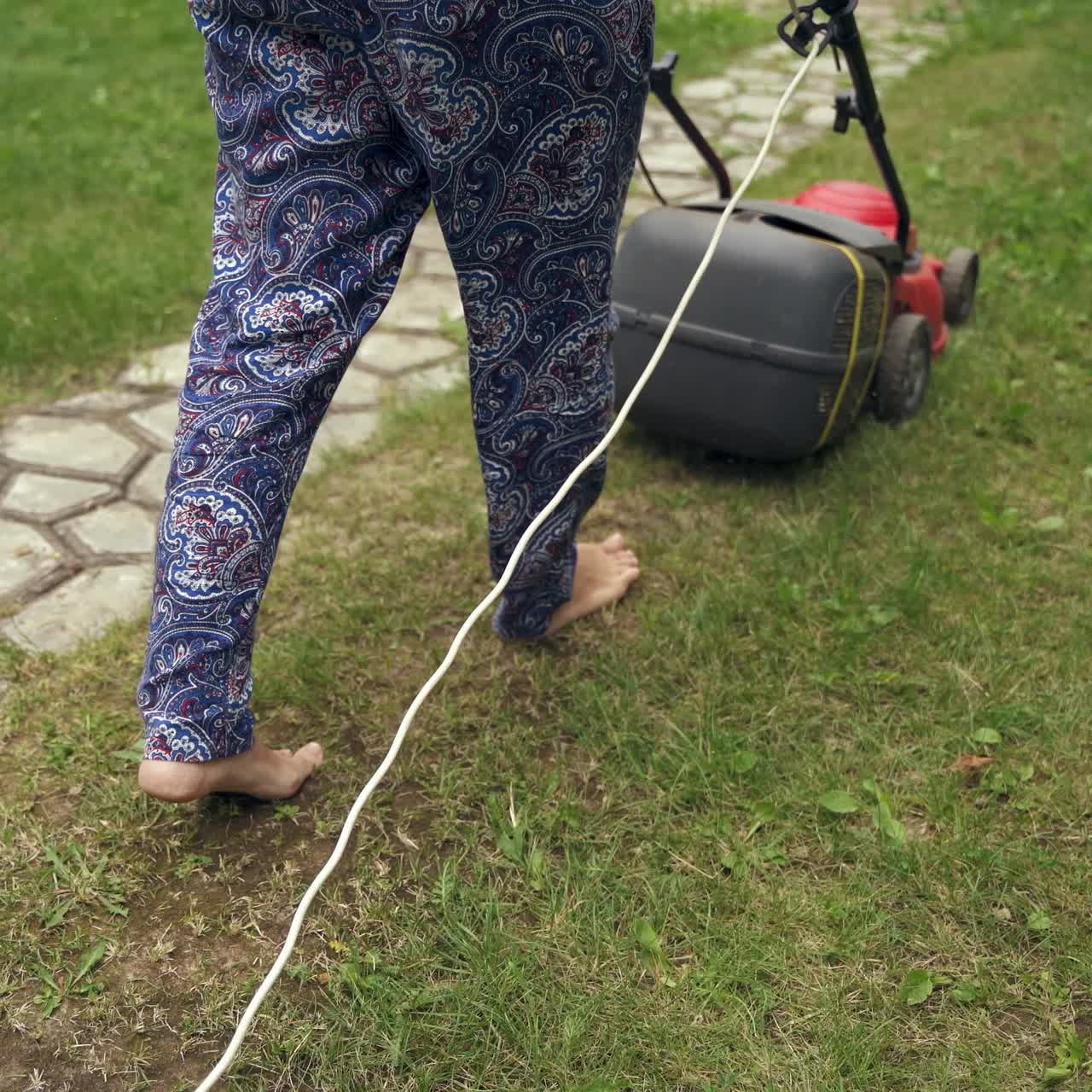 Woman's legs and corded lawn mower. Worker cutting grass in the garden. Gardening activity. Female worker pushing mowing machine.