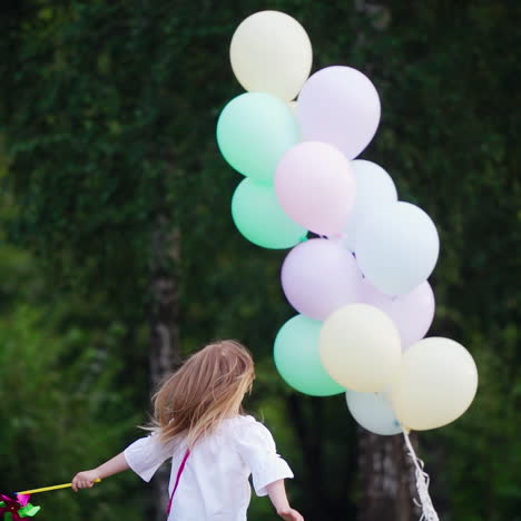 back view of a little girl in the park. small girl in blue jeans runs to the lots of air balloons on the natural green background in summer.