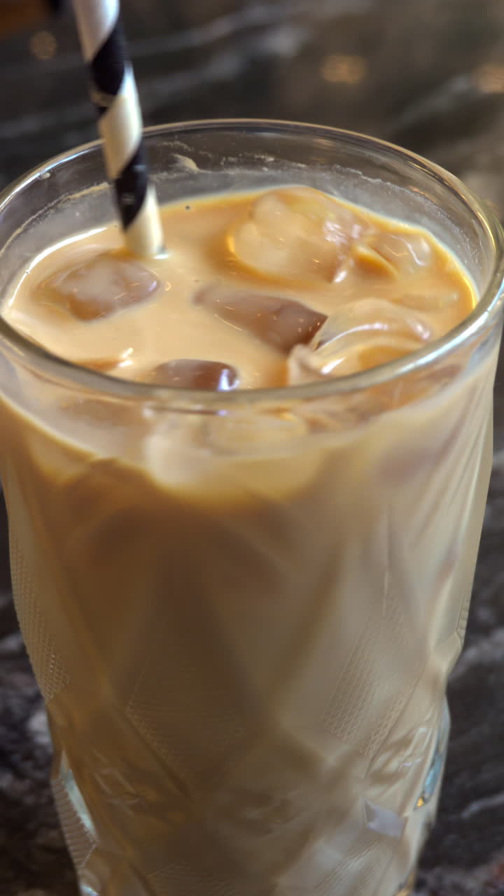 Close up of an iced latte being swirled with a straw. Vertical