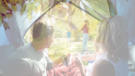 camping couple drinking coffee over family playing soccer in park