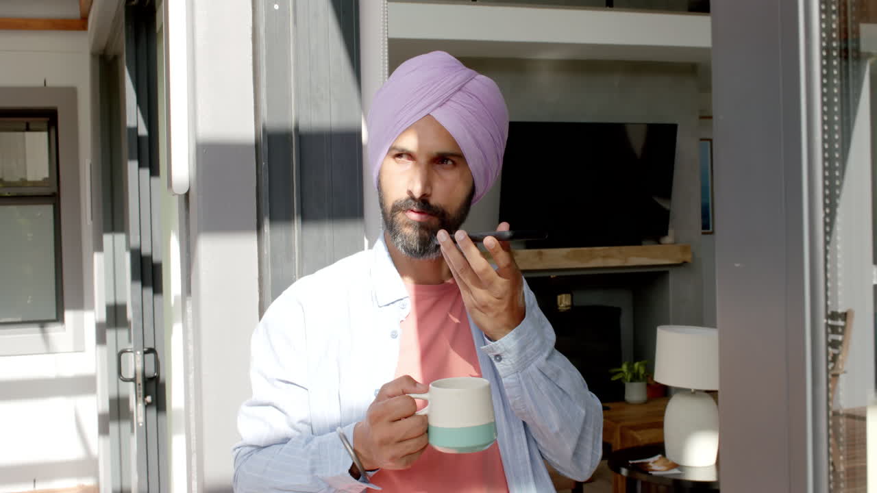 Holding cup, man in turban speaking on smartphone in modern home setting