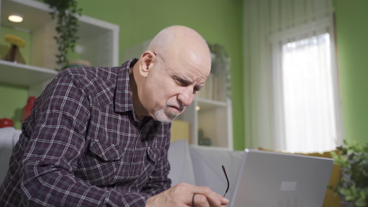 Old man working at home on laptop, doing research, writing mail.