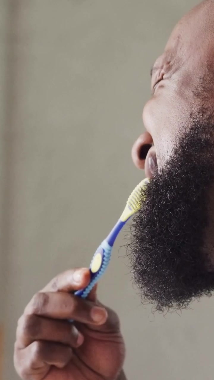 Vertical video: Raising blue brush, bearded man brushing at sink in tank with foam to clean teeth