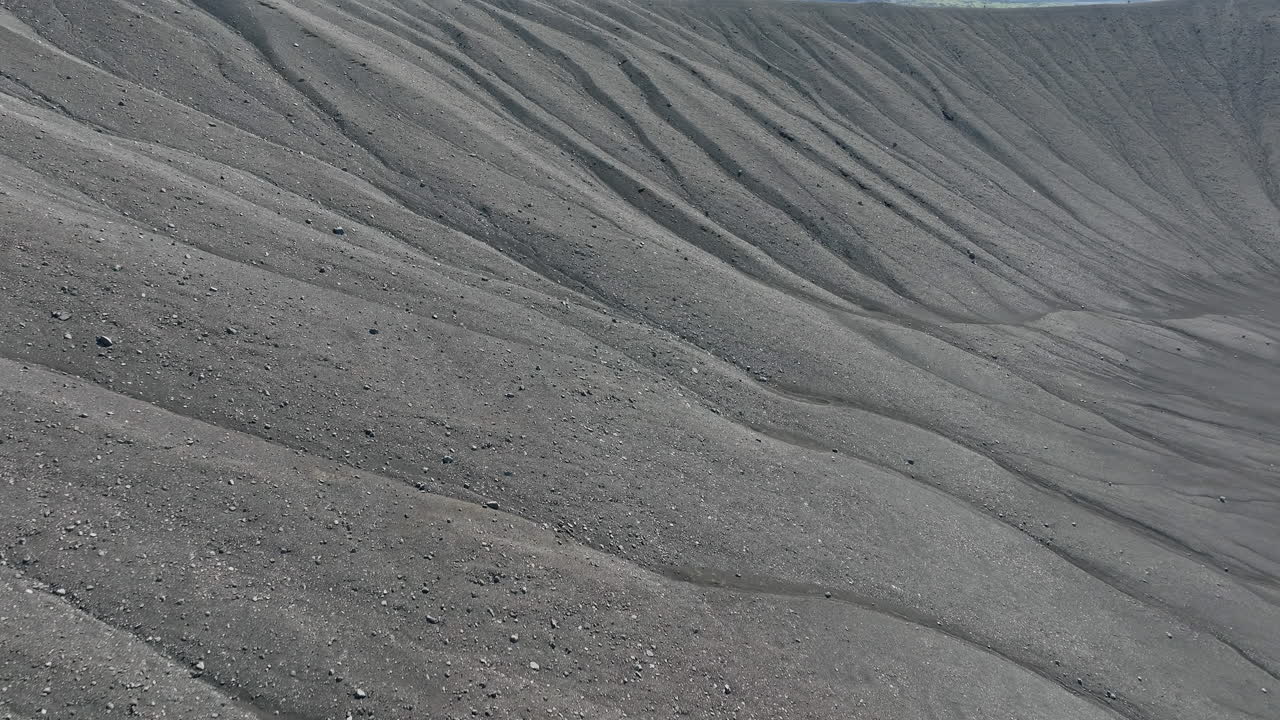 Black volcanic sand surface on the crater rim, close up aerial view