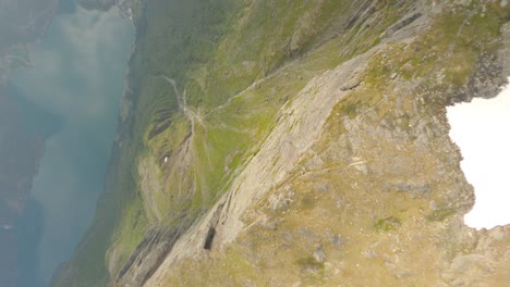 Vuelo-Fpv-Cuesta-Abajo-Desde-La-Cima-De-La-Montaña-En-Dirección-Valle-Con-Fiordo-En-Noruega---Con-Vistas-A-La-Ciudad-De-Odda-Desde-La-Montaña-Rossnos