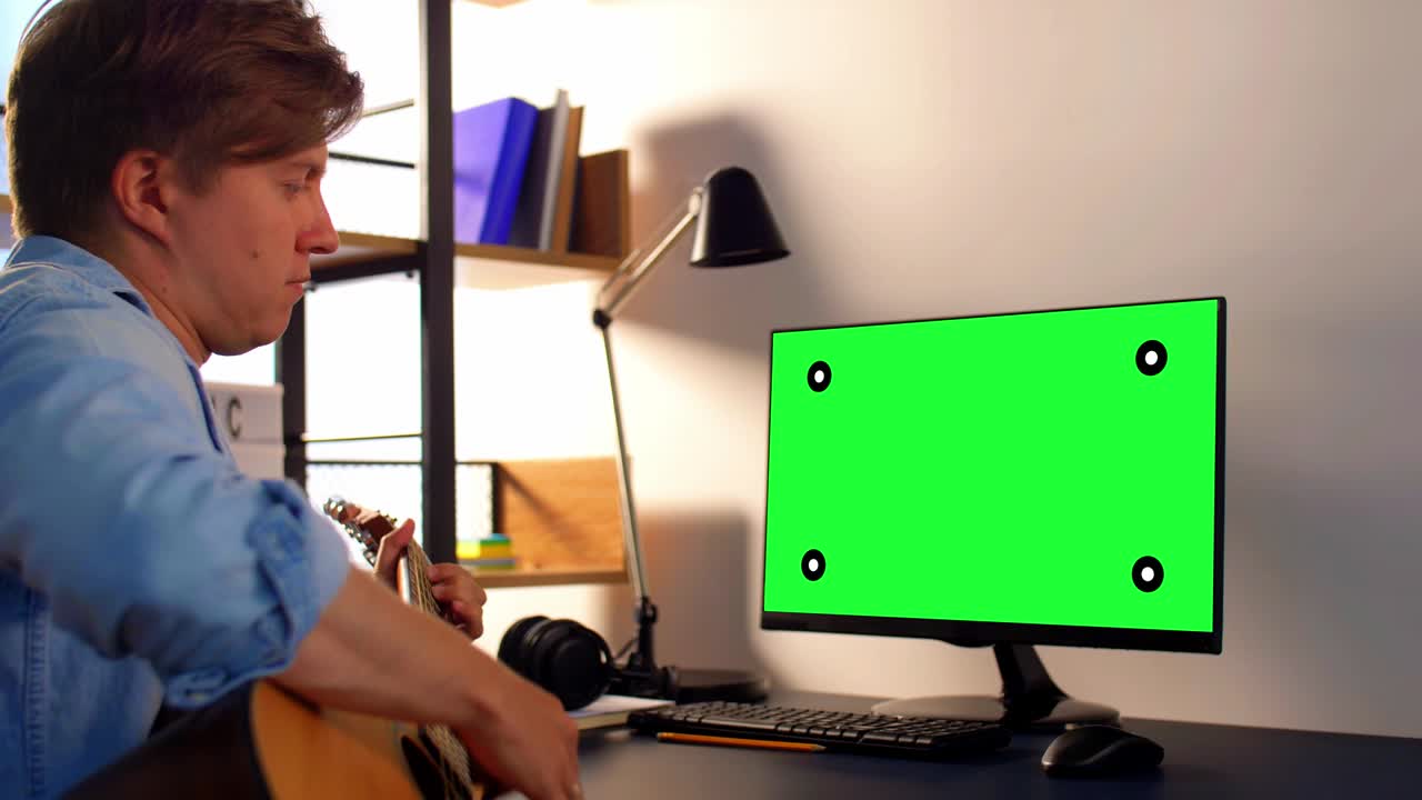 joven con computadora tocando la guitarra en casa