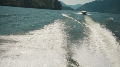 splashing trail on sea water and sailboat in sunny lagoon slow motion. white trace on surface against distant motorboat at tropical resort. marine scene