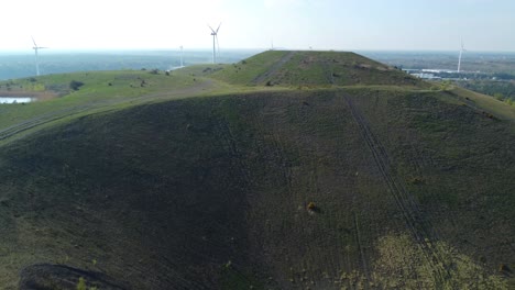 High-mining-heap-with-wind-turbine-farm-behind,-aerial-drone-view