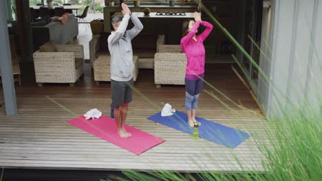 happy diverse couple doing yoga, standing and meditating at terrace