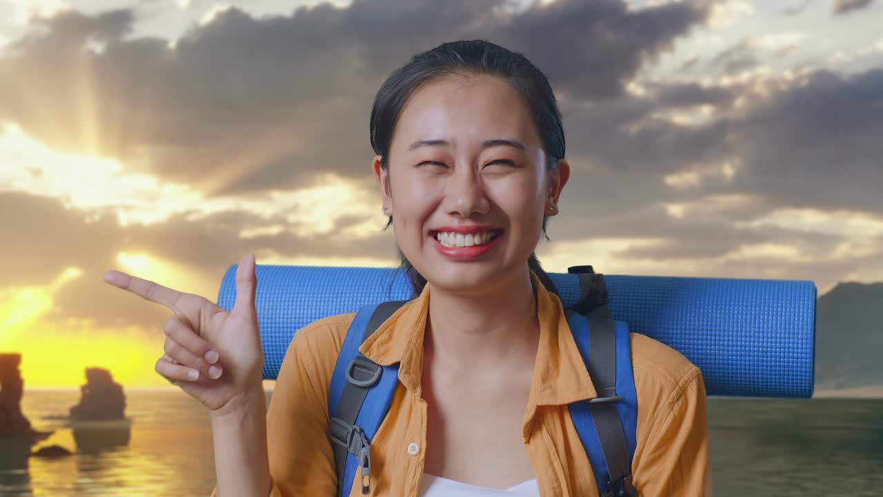 夕焼け時のビーチに立ち、笑顔で横を指さす登山用バックパックを背負ったアジア人女性ハイカーのクローズアップ