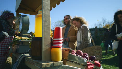 couple standing at the stall with fruits and vegetables adult couple standing at the stall with fruits and vegetables people walking and shopping on background local farmers market or fair outdoors vegetarian and organic food agriculture
