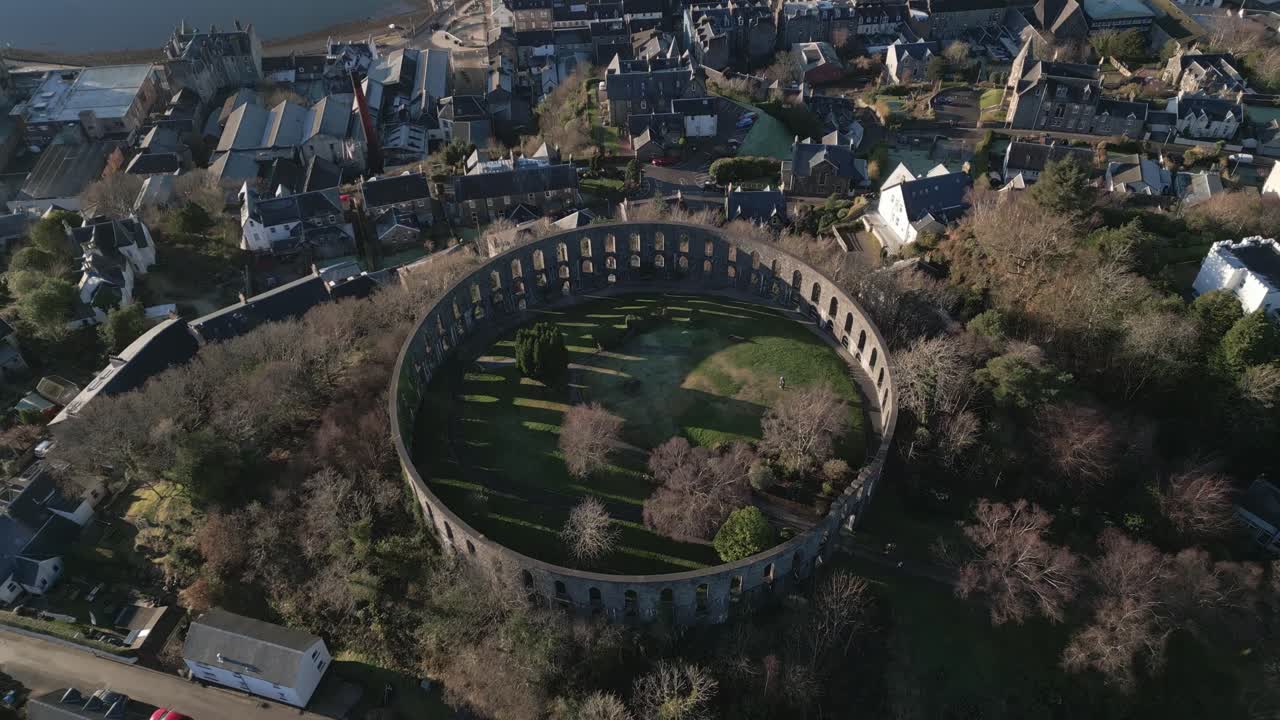 Aerial view of Oban and Mccaig's Tower and Battery Hill in the low winter sun. Drone ascending camera tilting down