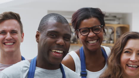 portrait of smiling men and women wearing aprons taking part in kitchen cookery class