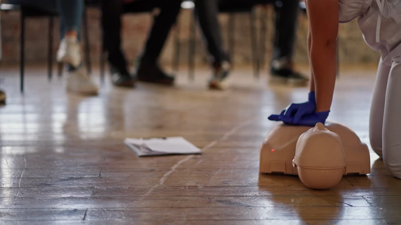Close-up shooting from the bottom: A professional female doctor conducts a practical training in medical care, performing artificial respiration on a mannequin for the public